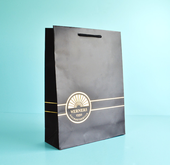 custom printed black rope handle paper bag with gold logo on blue background